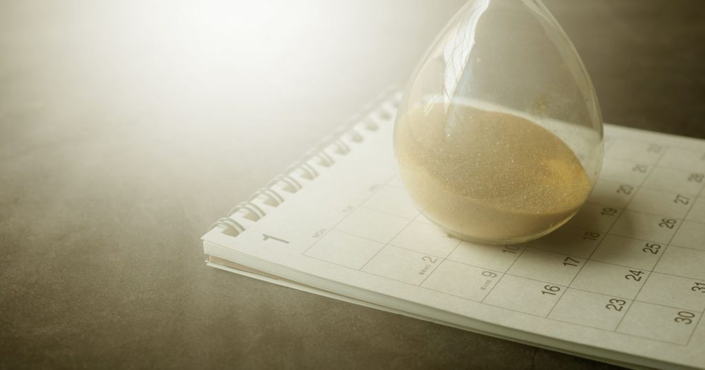 An hourglass resting on a paper calendar, representing the months a nonprofit waits for the IRS to approve its 501(c)(3) application.