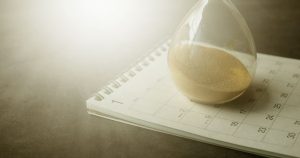 An hourglass resting on a paper calendar, representing the months a nonprofit waits for the IRS to approve its 501(c)(3) application.